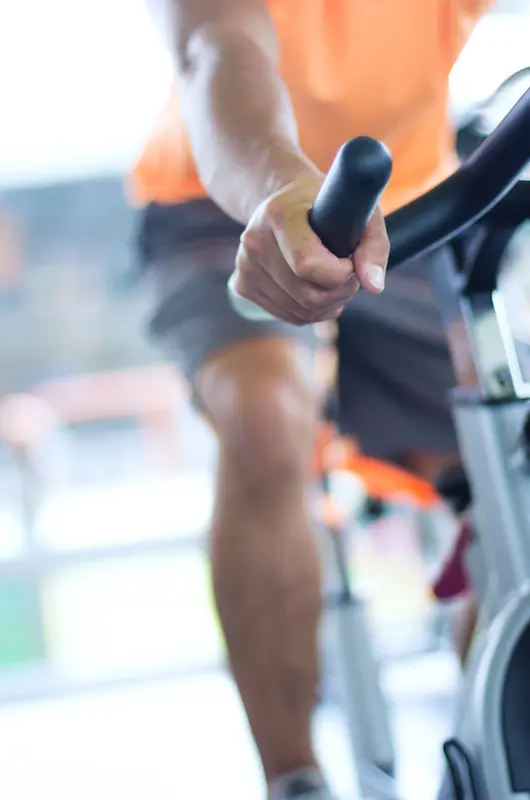 Person cycling on an exercise bike, emphasizing the cardiovascular benefits of aerobic exercise, including improved heart endurance, lower blood pressure, and enhanced lipid profile.